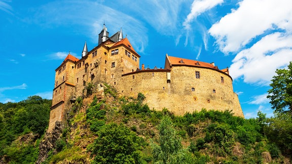 Burg Kriebstein bei Waldheim thront auf einem Felsen über einem Fluss, dahinter blauer Himmel