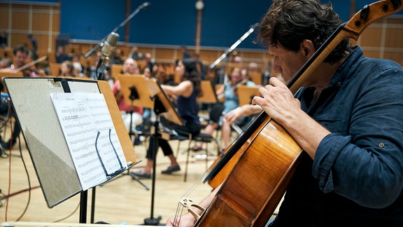 Blick in ein Orchester während der Probenarbeit. Im Vordergund spielt ein Mann auf dem Cello.
