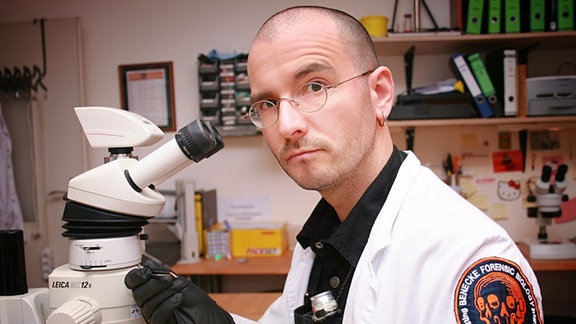 ein Mann mit Brille vor einem Mikroskop