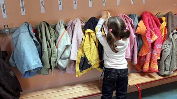 Ein Mädchen hängt ihre Jacke in der Garderobe eines Kindergartens auf.