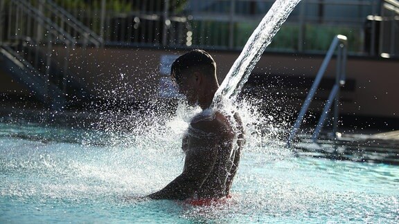Bester Platz bei Hitze: Ein Mann kühlt sich im Freibad unter einer Wasserdusche ab