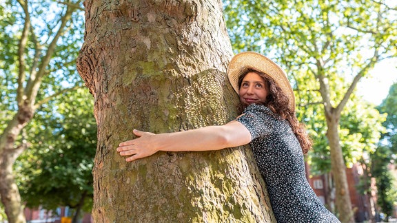 Junge Frau, die einen Baum im Park umarmt