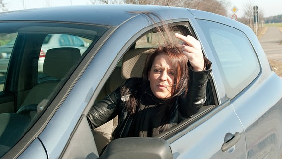 Eine Frau zeigt aus dem Autofenster heraus jemandem den Mittelfinger