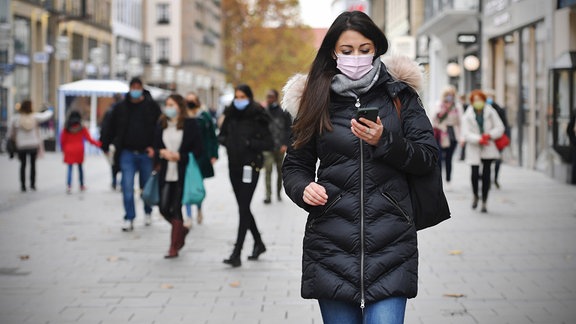 Junge Frau mit Maske und Smartphone in der Fußgängerzone
