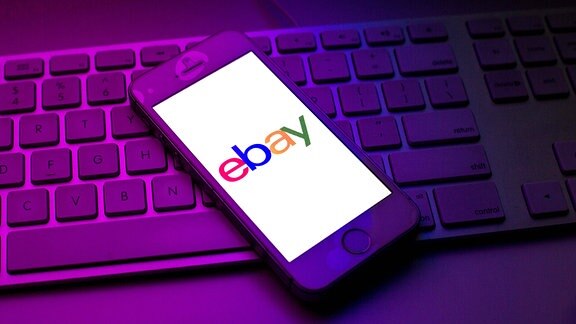 Das Ebay Logo ist auf einem Handy zu sehen, das auf einet Tastatur liegt.