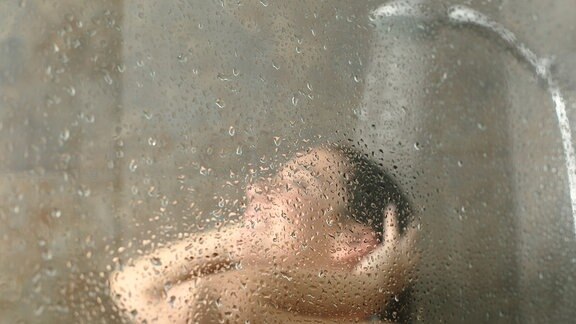 Duschen macht kreativ, sagen Forscher! Im Bild duscht eine Frau, zu sehen durch die wasserbenetzte Scheibe.