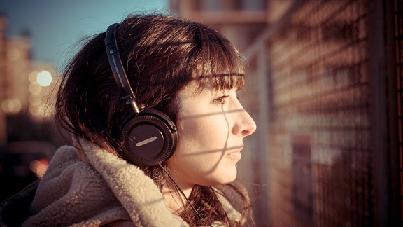 Eine Studie hat herausgefunden, dass es immer weniger traurige Musik gibt. Im Bild ist eine brünette Frau zu sehen, die traurig in Richtung Sonne blickt und Kopfhörer auf hat.