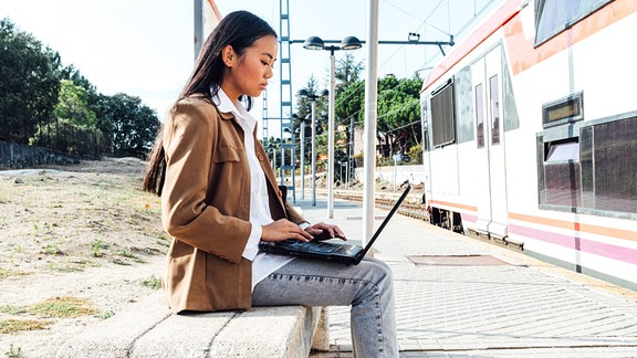Eine Frau arbeitet am Laptop und wartet auf ihren Zug