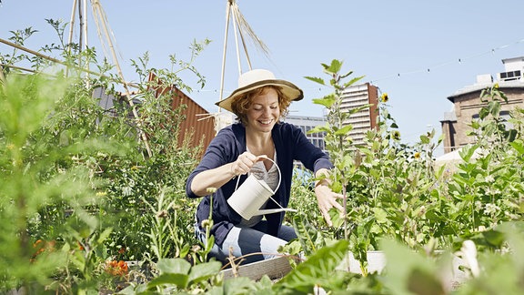 Eine Frau gießt ihre Pflanzen im Garten und lächelt dabei.