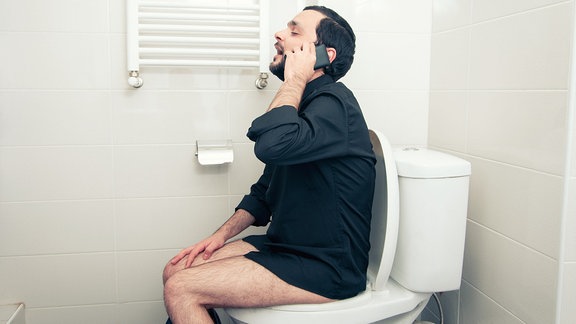 Mann sitzt auf der Toilette und telefoniert