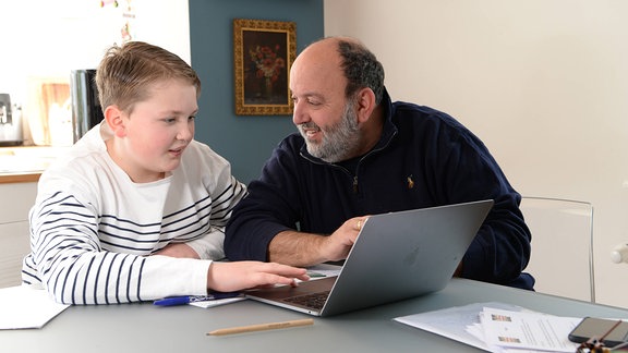 Homeschooling: Vater sitzt mit seinem Sohn vor einem Laptop und hilft seinem Sohn bei den Schulaufgaben, die  während der Schulschliessung wegen der Coronavirus-Krise zu Hause erledigt werden müssen.