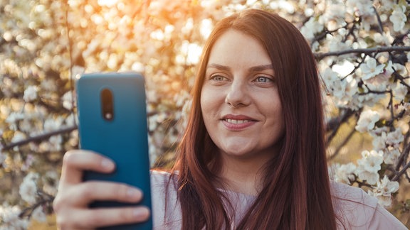 Eine junge Frau hält sich ein Smartphone vors Gesicht
