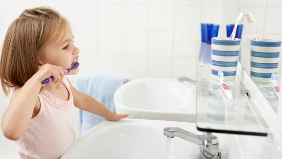 Ein Kind putzt vorm Spiegel stehend Zähne