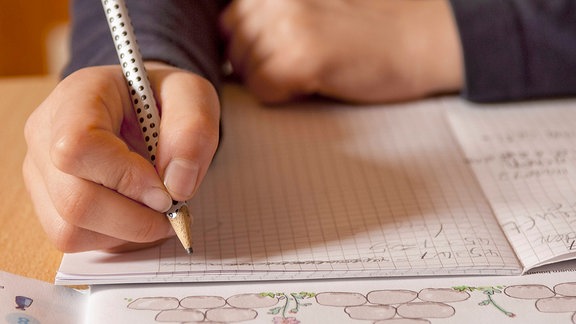 Schulkind schreibt mit Bleistift in ein Heft (Symbolbild)