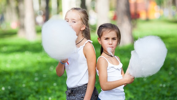 Statistisch gesehen verzehrt jeder Deutsche mehr als 34 Kilogramm Zucker pro Jahr. Auf dem Bild essen zwei junge dunkelhaarige Mädchen Zuckerwatte im Park.