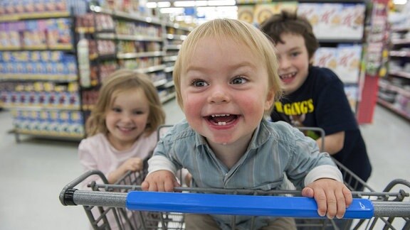 Drei Kinder haben Spass mit Einkaufswagen im Supermarkt