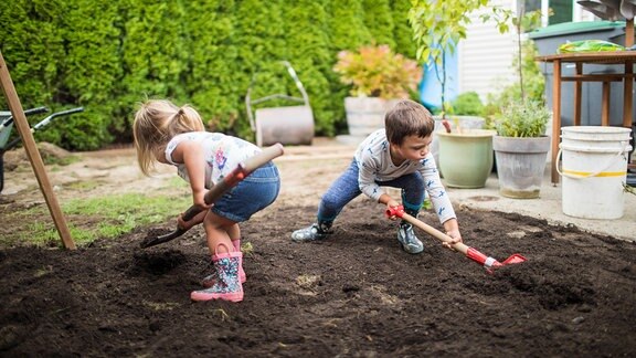 Zwei Kinder schaufeln Erde im Garten (Symbolfoto)