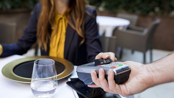Eine Frau bezahlt im Restaurant kontaktlos mit Karte
