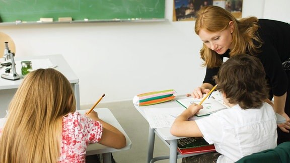 Eine Lehrerin hilft zwei Schülern bei ihren Aufgaben.