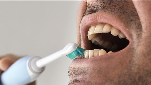 Ein Mann Putzt sich die Zähne mit einer Elektrischen Zahnbürste.