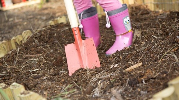 Mädchen mit rosa Gummistiefeln beim Umgraben im Garten