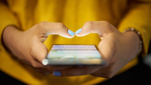 Die SMS wird am 3. Dezember 2017 25 Jahre alt. Mit dem Smartphone tippt eine Frau in einer gelben Bluse eine Textnachricht.