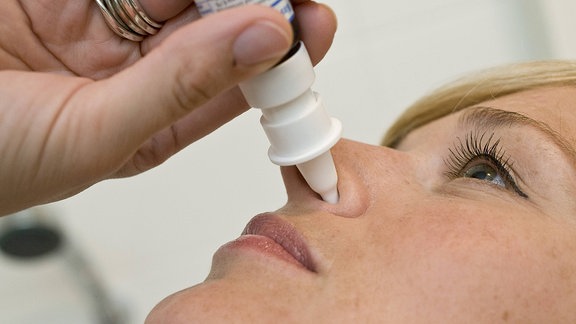 Eine Frau sprüht sich Nasenspray in die Nase.