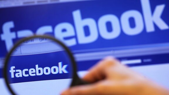 Durch eine Lupe ist der Schriftzug des sozialen Internet-Netzwerks Facebook auf einem Laptop zu sehen.