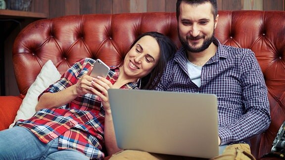 Ein Paar auf dem Sofa mit Laptop und Handy