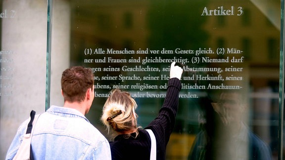 Ein Paar liest Teile des Grundgesetzes, das in die Glaswände des Jakob-Kaiser-Hauses in Berlin graviert wurde