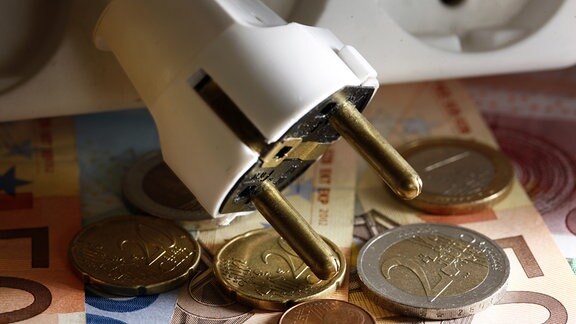 Der Stecker einer Mehrfachsteckleiste liegt auf Euro-Geldscheinen und Münzen