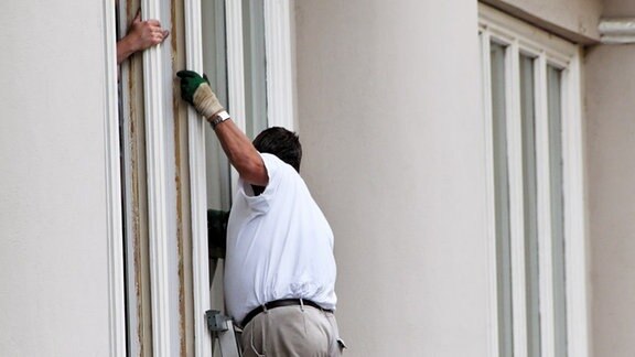 ein Bauarbeiter wechselt an einem Haus die Fenster aus