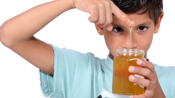 Ein kleiner Junge steckt seinen Finger in ein Honigglas