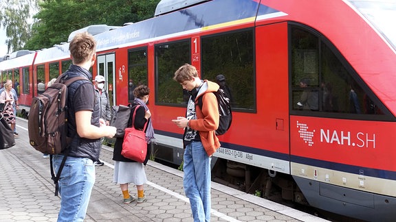 Ein Regionalexpress fährt im Juli 2022 auf einem Bahnsteig ein. Pendler warten. (Symbolbild)