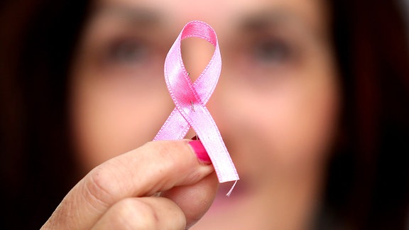 Eine Frau hält die Rosa Schleife gegen Brustkrebs in die Kamera
