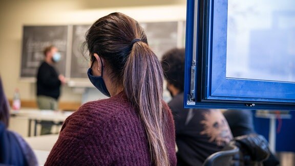 Eine Schülerin sitzt mit Maske vor offenem Fenster und folgt dem Unterricht.