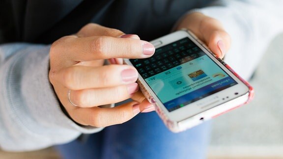 Frau mit rosa Fingernägeln hält ein Smartphone, auf dem Bildschirm sind Icons zu sehen