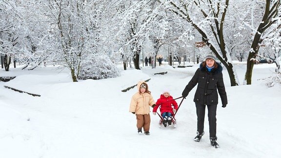 Eine Mutter mit zwei Kindern beim Winterspaziergang in einem verschneiten Park